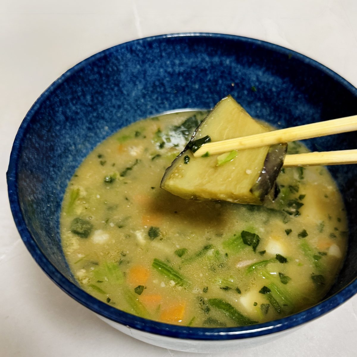 GREEN SPOONのスープ Tadaima（西京味噌の野菜たっぷり豚汁）。青い器に盛り、なすを箸で持ち上げたところ